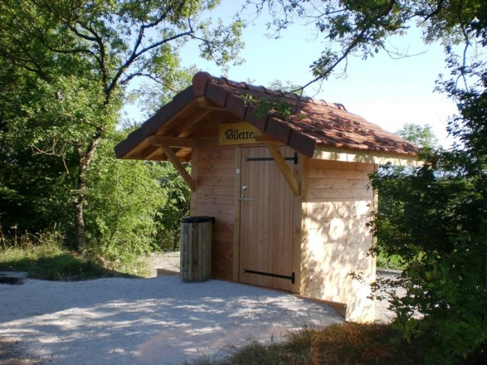 Une toilette sèche avec une poubelle bois devant