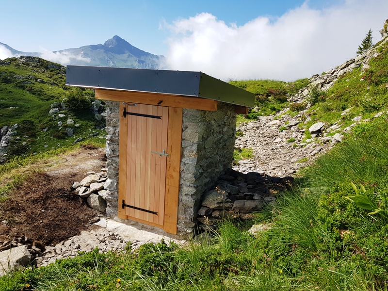 On voit la toilette de la bergerie de Prarian en pierre maçonnée depuis l'avant avec vue sur les montagnes