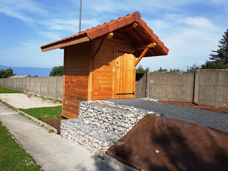 La toilette sèche est insatllée devant des gabions et une rampe en gravier